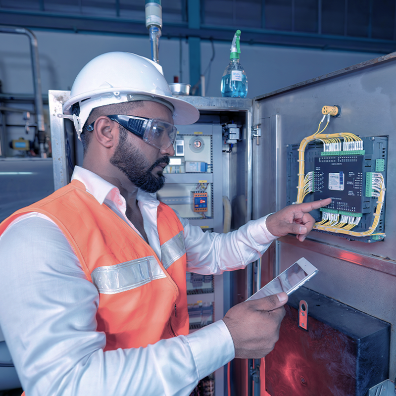 Technicien en gilet haute visibilité et casque de sécurité inspectant un panneau de contrôle électrique dans un environnement industriel
